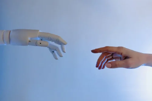 Image d'une main humaine tendue vers celle d'un robot - SEO et IA - Lemon Interactive